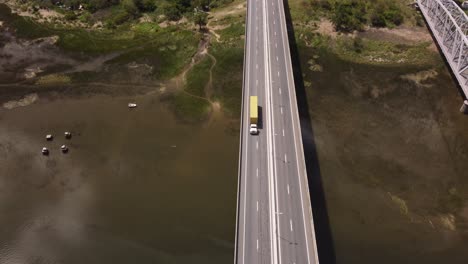 Toma-Aérea-De-Un-Camión-Amarillo-Conduciendo-En-El-Puente-Barra-De-Santa-Lucía-Durante-Un-Día-Soleado-En-Uruguay