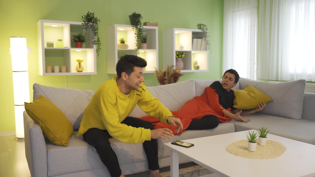 어색하고 재미있는 젊은이가 집의 소파에 누워 있는 남자친구에게 뛰어들어 그를 알아차리지 못하고 그의 친구는 화를 내고 있습니다.