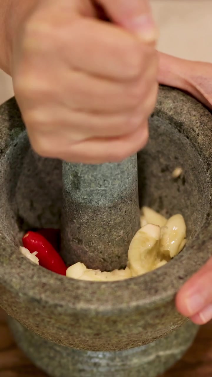 Mani schiacciano aglio e peperoncino in un mortaio di pietra, creando una pasta vivace e aromatica.