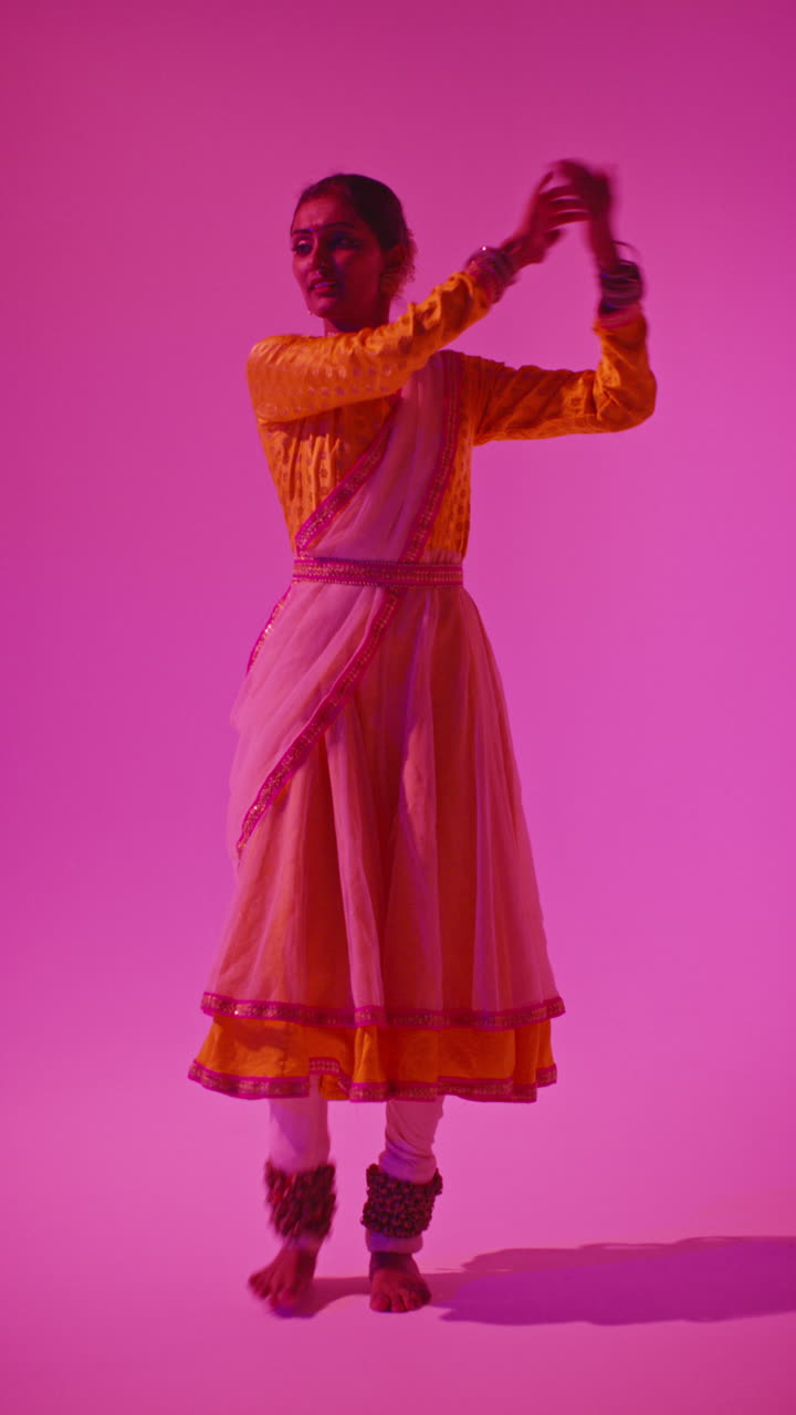 video vertical de larga duración en estudio de una bailarina de kathak que realiza un baile vestida con el vestido tradicional indio contra un fondo púrpura 7