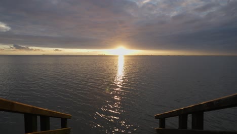 Incline-Hacia-Arriba-Desde-Las-Escaleras-De-Madera-Que-Conducen-Al-Mar-Del-Norte-Hasta-El-Sol-Dorado-Sobre-El-Horizonte,-El-Cielo-De-La-Puesta-De-Sol-Frente-Al-Mar-Con-Nubes-Densas-Dramáticas