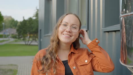 Süße-Frau-Repariert-Haare,-Bürstet-Sie-Hinter-Dem-Ohr-Und-Starrt-Aufmerksam-Und-Zielstrebig-Nach-Vorne,-Vorstädtischer-Hintergrund