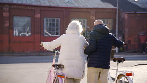 vista posteriore di una coppia anziana che cammina tenendo le bici in strada in una giornata invernale