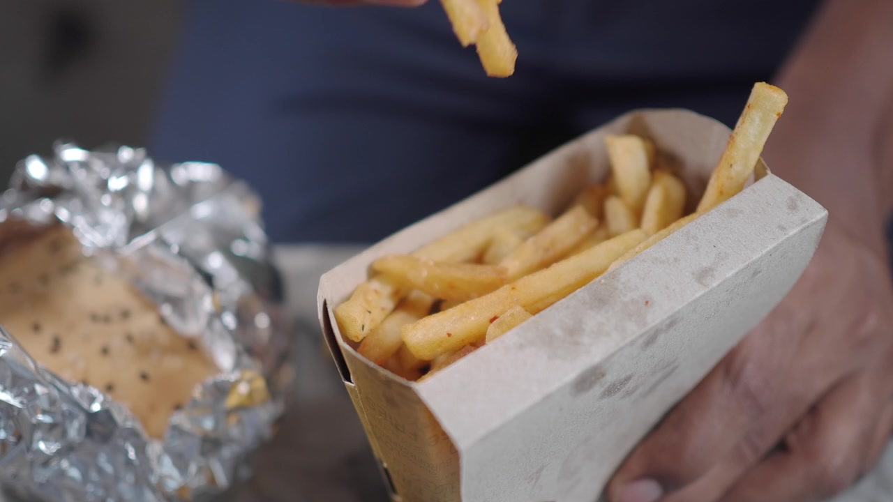 Close-up of a Hand Picking a French Fry from a Cardboard Container