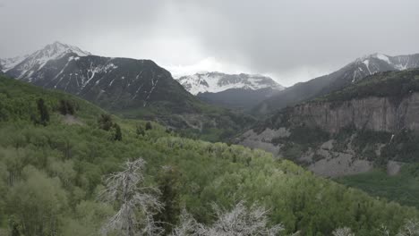 colorado rocky mountains with stormy grey clouds close to a highway, aerial flyover shot