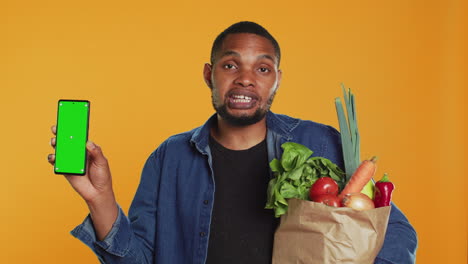 Young-adult-holding-a-smartphone-with-greenscreen-layout-in-studio