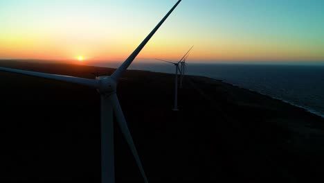 Wind-turbine-silhouette-as-last-light-from-sunset-dips-below-ocean,-push-in-past-large-blades