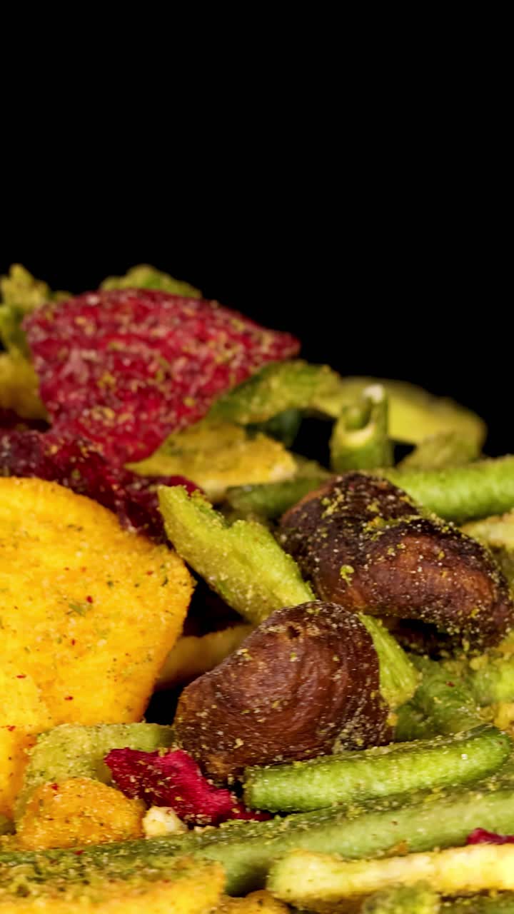 Colorate chips di verdure disidratate ruotano sotto le luci dello studio, rivelando consistenze croccanti e dettagli vivaci