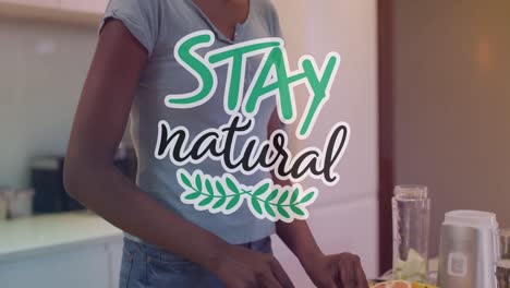 Animation-Des-Textes-„Stay-Natural“-über-Einer-Afroamerikanerin,-Die-Obst-Schneidet
