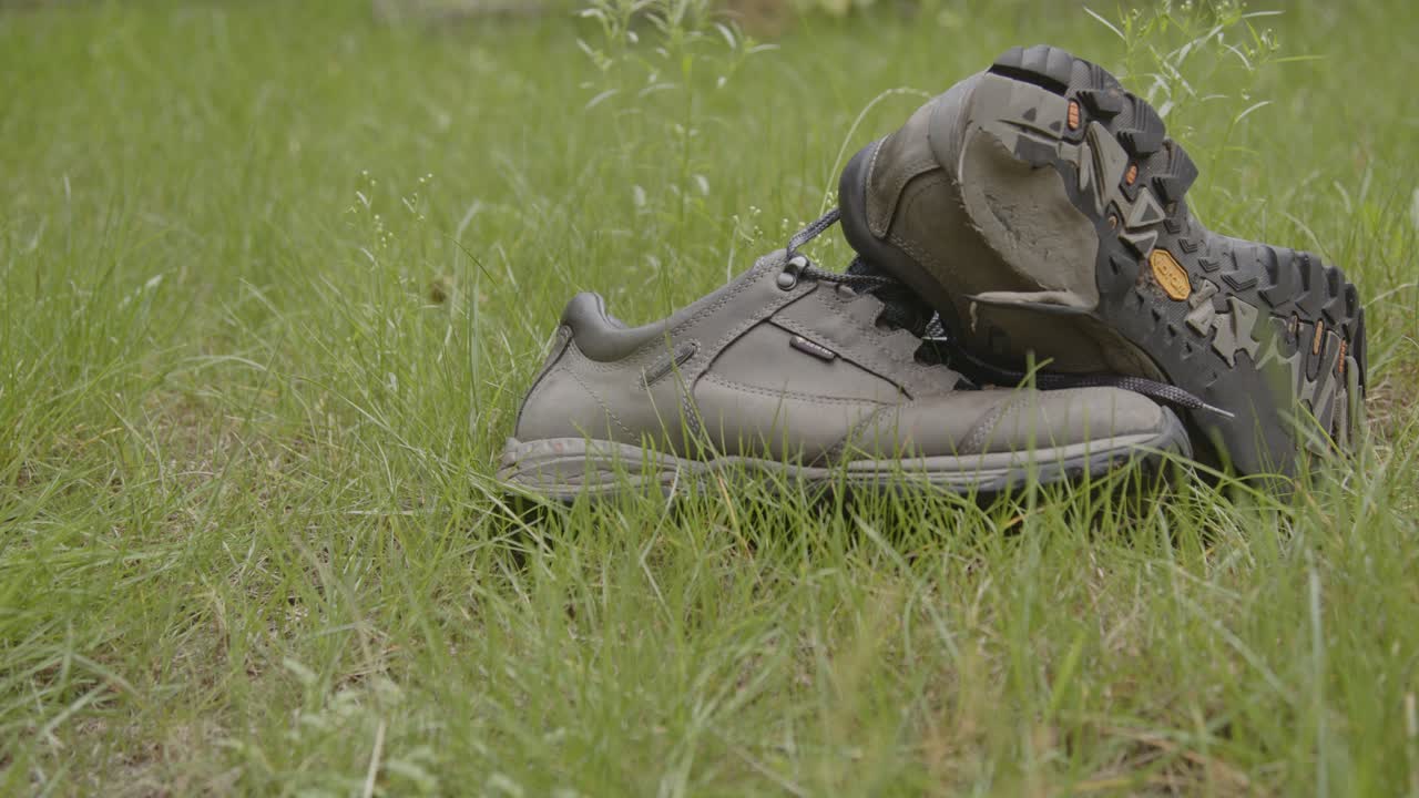 Dolly of pair of old hiking shoes lying in a field of grass