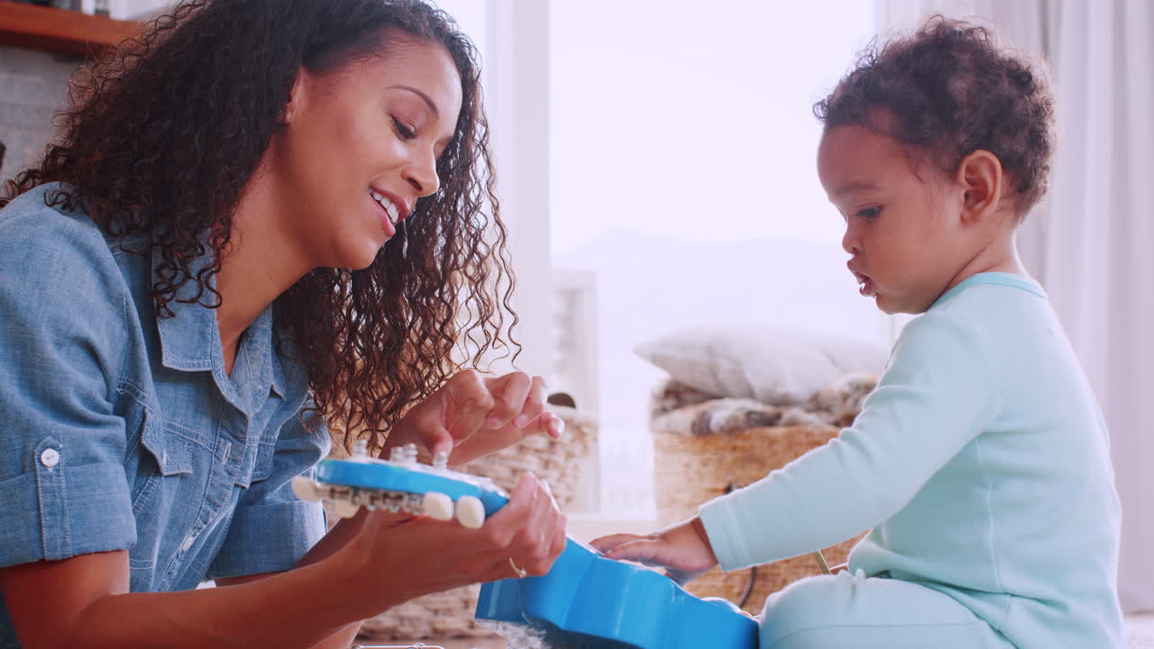 joven madre negra y su hijo tocando el ukelele en la sala de estar