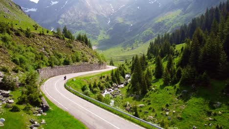 drone tracks biker riding through transfăgărășan road in carpathian mountains of romania, surrounded by lush greenery and alpine landscape