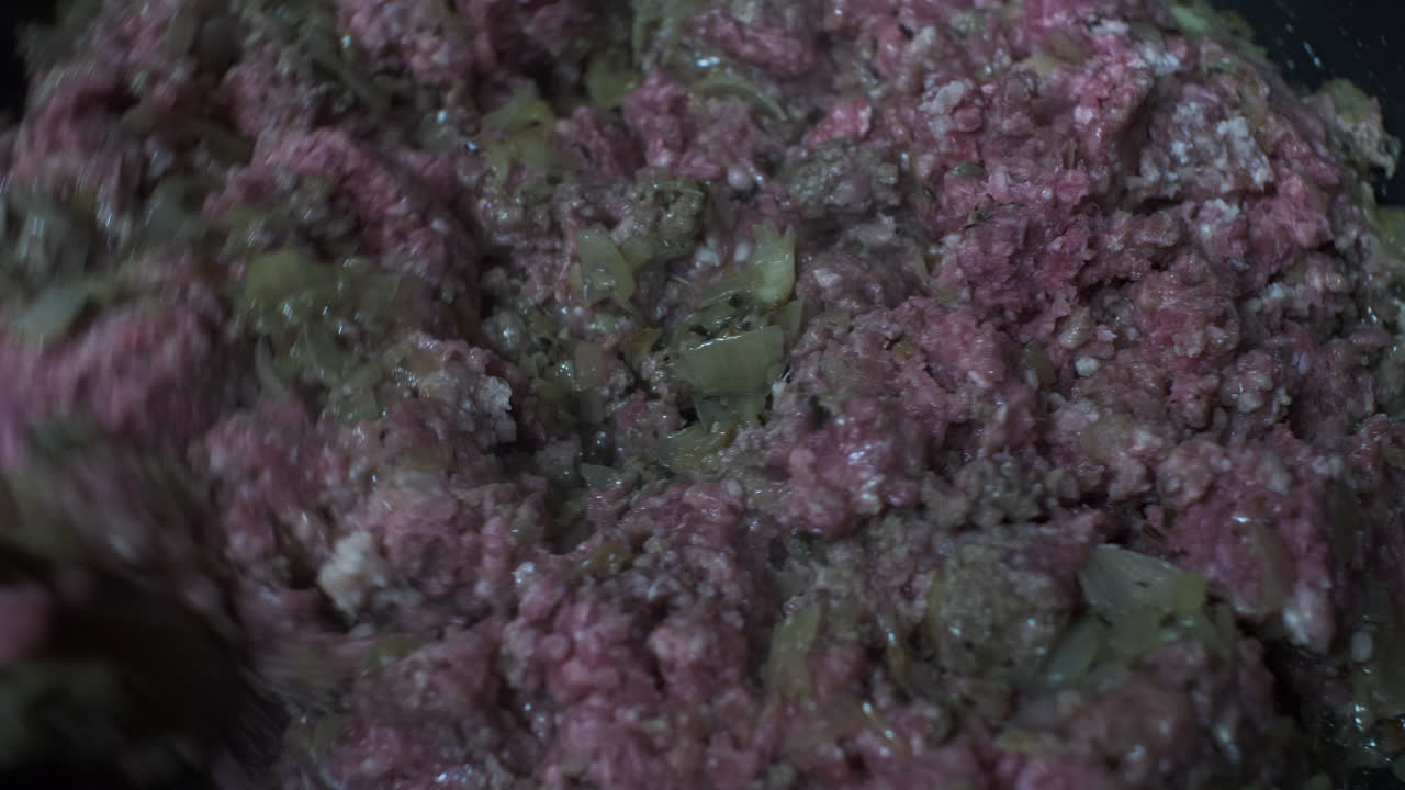 carne molida cruda revuelta con una cuchara de madera en una sartén