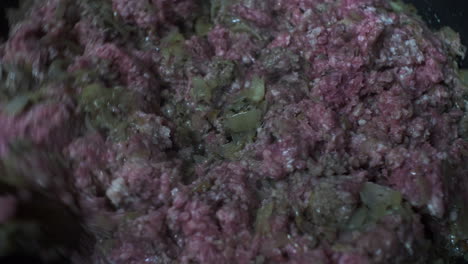 raw ground beef being stirred with wooden spoon in frying pan