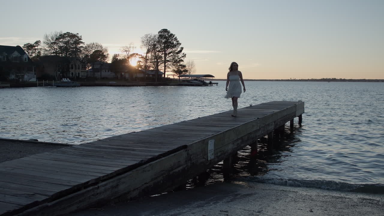 Bella ragazza che si allontana da un molo al tramonto.