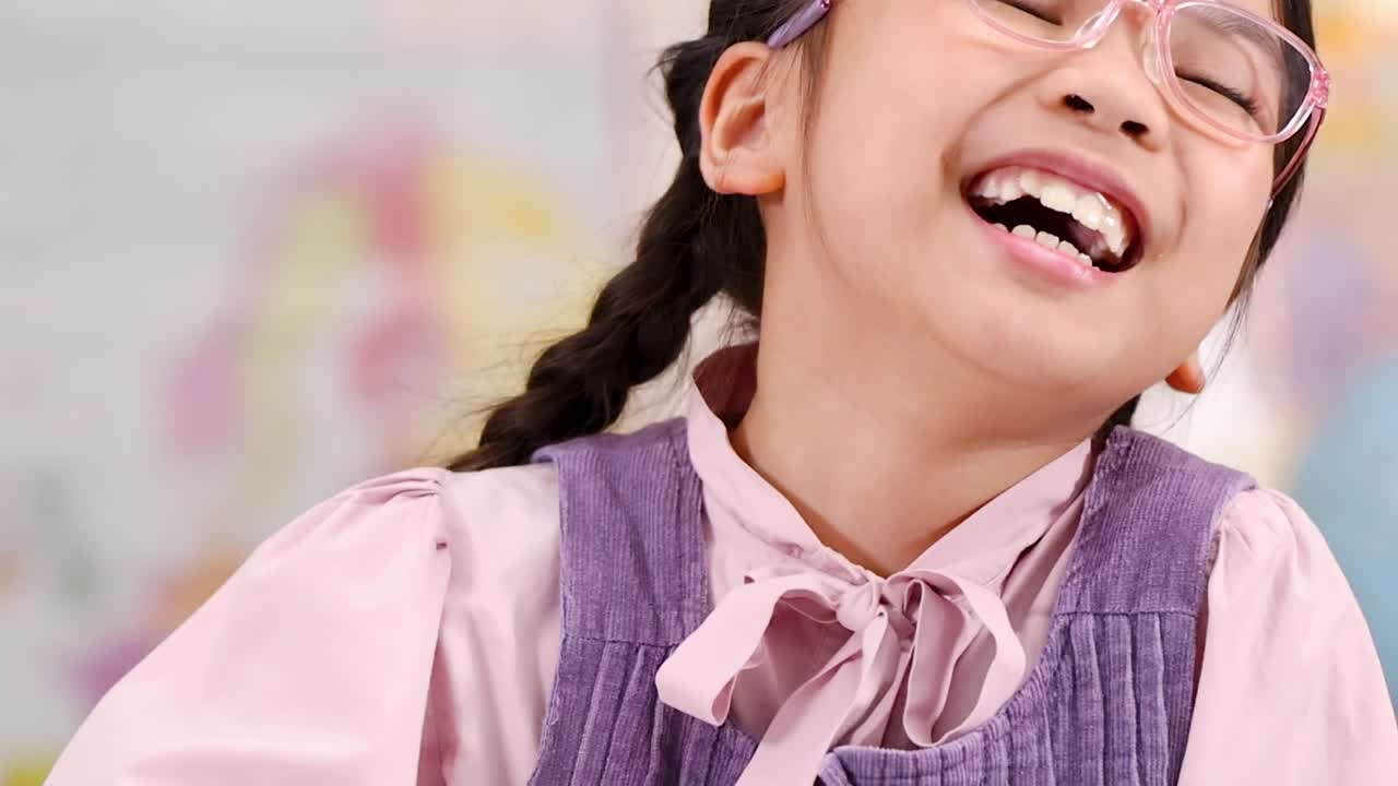 明るい教室で、編み込みの髪をした陽気な少女が静かにする仕草をしている