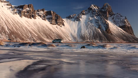 vista aérea de la furgoneta que se desplaza por una carretera nevada en el área de vestrahorn islandia, revelando un espectacular paisaje salvaje de invierno, vastas tierras y la famosa montaña rocosa de vestrahorn