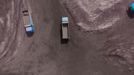 aerial top down view of dump trucks drive on dusty coal mine site road