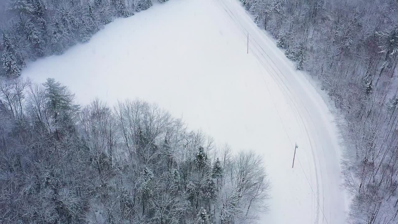 숲과 들판을 따라 구불구불한 도로가 있는 눈 덮힌 풍경 위를 날아가는 공중 탑다운
