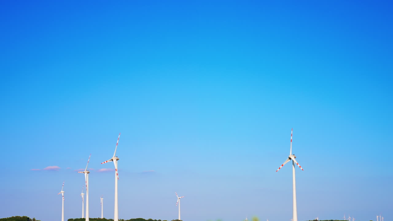 Turbines against blue sky. Multiple wind turbines spin gently under a bright blue sky beside a green landscape, showcasing renewable energy