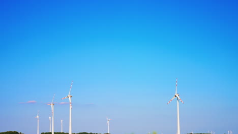 turbines against blue sky. multiple wind turbines spin gently under a bright blue sky beside a green landscape, showcasing renewable energy