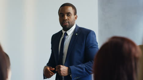 Close-up-view-of-african-american-businessman-speaker-on-a-podium-wearing-formal-clothes-and-talking-in-a-conference-room-in-front-to-many-people