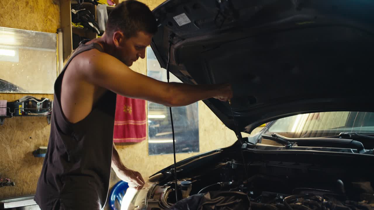 un maestro automovilista mecánico con un corte de pelo corto en una camiseta gris comprueba el capó del coche y el aceite allí en su taller de garaje. reparación de capó de coche en mi taller