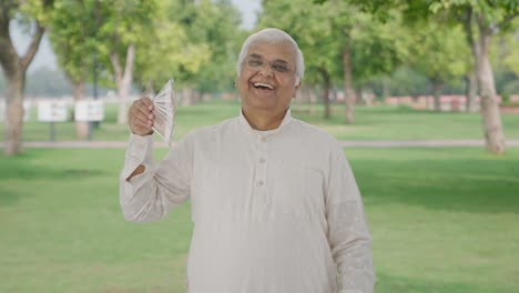 Happy-Indian-old-man-using-money-as-fan-in-park