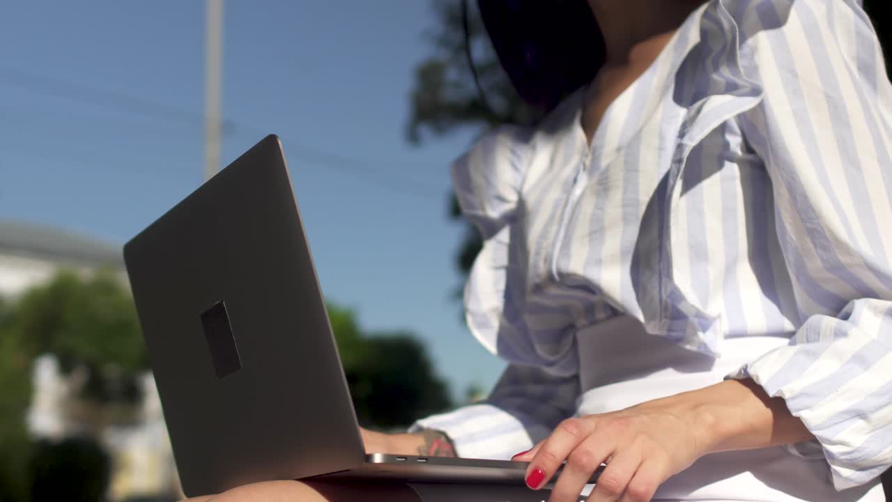 Stylish woman typing on laptop in park