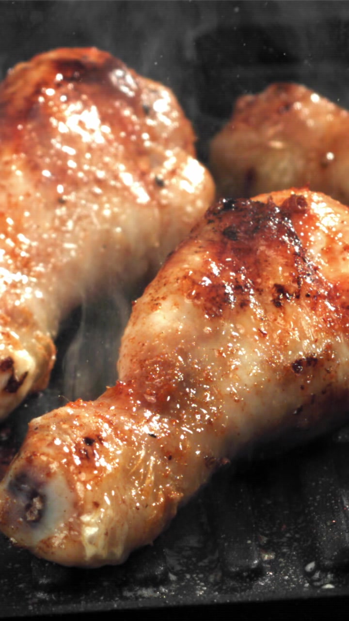 Fusi e cosce di pollo dorati che sfrigolano su una piastra.