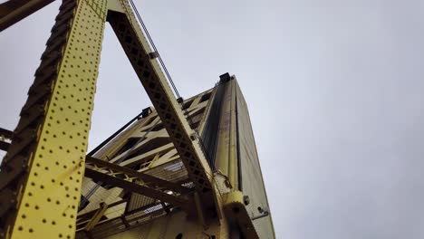 Cinematic-footage-looking-up-at-the-crossing-beams-of-the-yellow-bridge-in-downtown-sacramento,-california-with-a-grey-sky-in-the-background