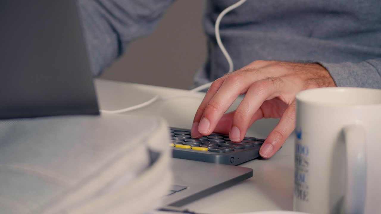Mani che usano una calcolatrice accanto a un computer portatile su una scrivania da ufficio con una tazza di caffè. Focus su finanza, gestione del budget, preparazione fiscale e attività di contabilità aziendale