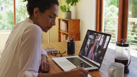 African-american-woman-taking-notes-while-having-video-call-with-female-colleague-on-laptop-at-home