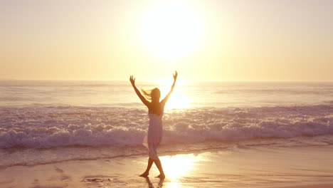 free happy woman with arms outstretched enjoying nature walking along beach at sunset face raised towards sky