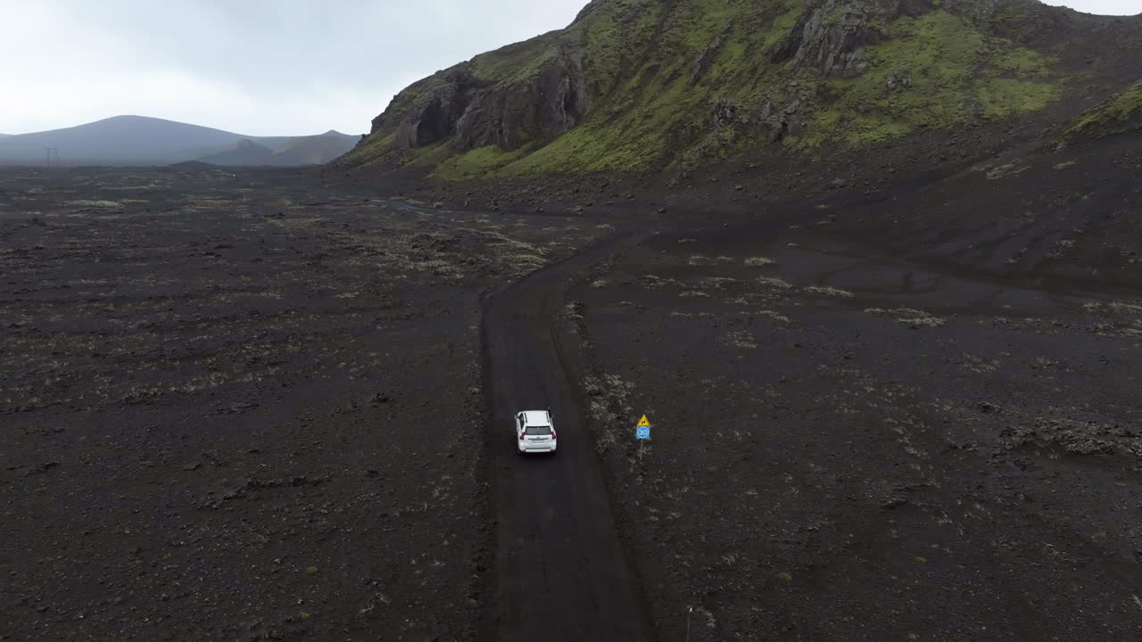 Aerial view circling a white SUV, driving in arctic wilderness of cloudy Iceland
