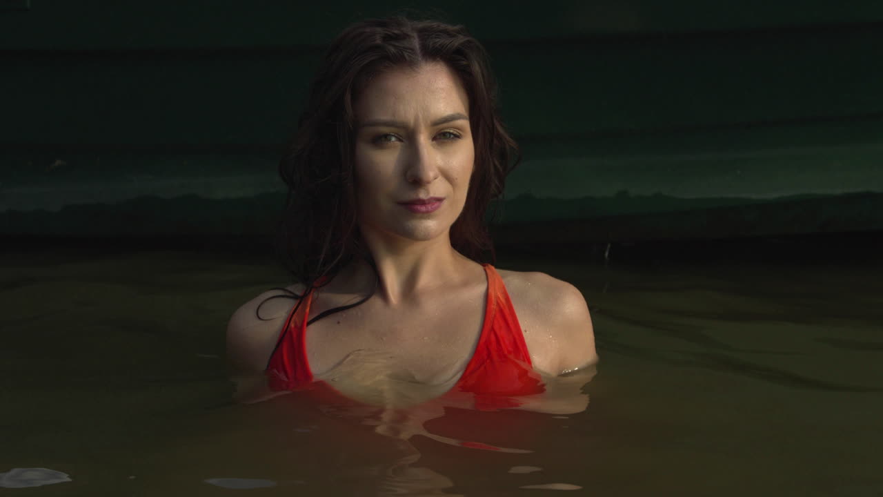 Ritratto di una bellissima giovane donna in bikini immersa fino al busto nel lago durante un meraviglioso tramonto