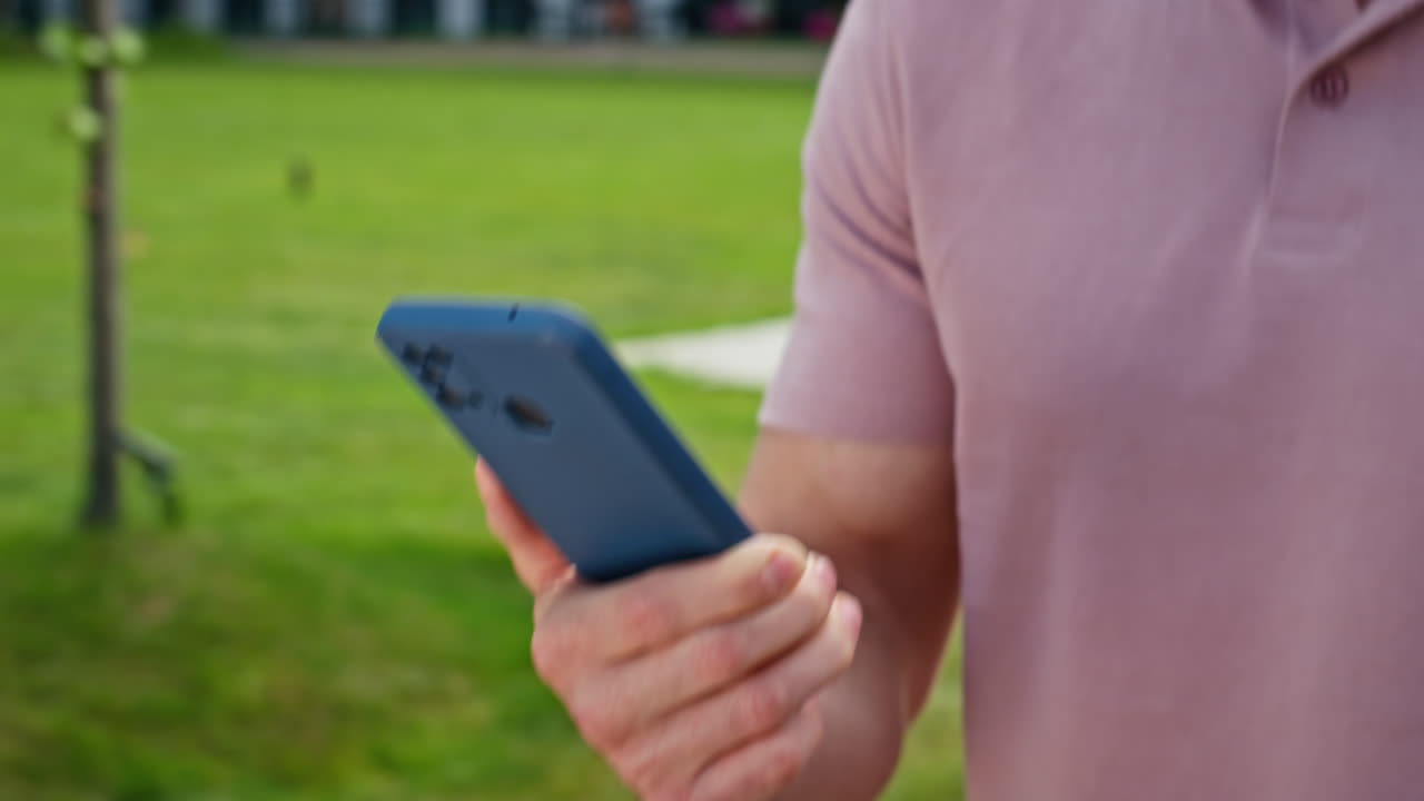 Guy holding smartphone walking green grass area closeup. Unknown businessman