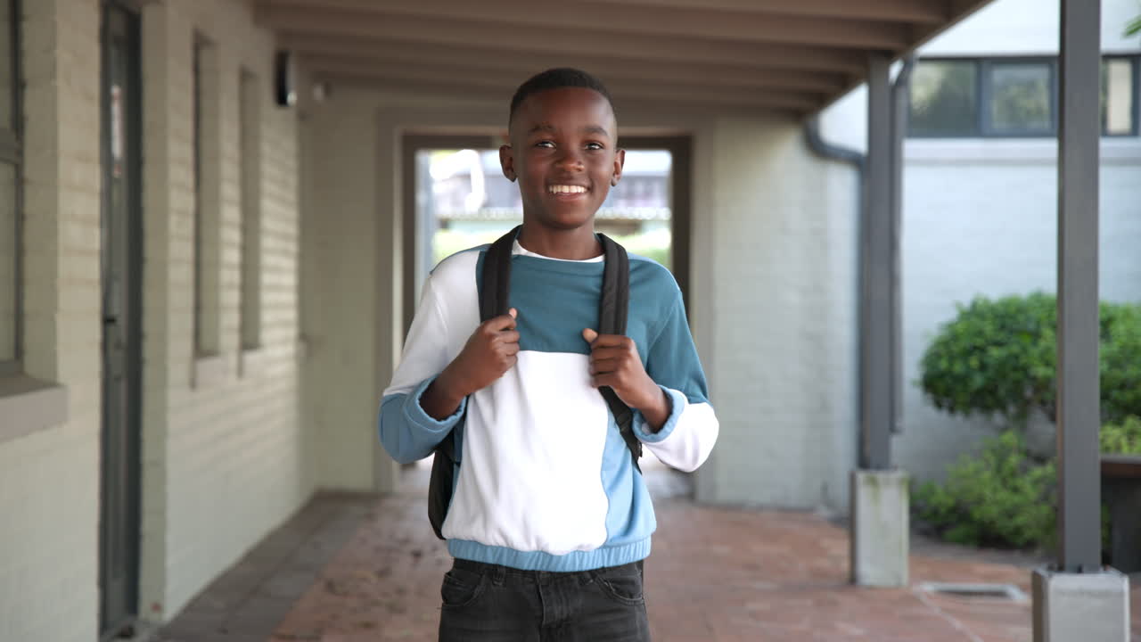 Ragazzo afroamericano entusiasta con lo zaino che sorride nel corridoio della scuola, godendosi la giornata, con spazio per il testo