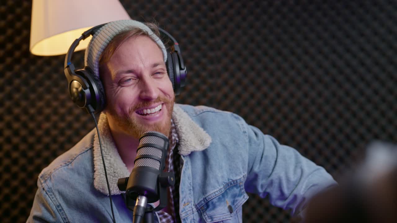 Guest on live radio or podcast show is listening to host nodding or shaking head. Good looking man with headphones and microphone in sound booth or professional recording studio is in an interview