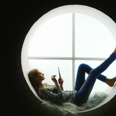 mujer relajada en una ventana redonda usa tableta