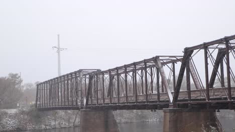 Old-wooden-and-steel-railroad-bridge-now-a-walking-path-in-In-Eau-Claire-Wisconsin's-phoenix-park-crosses-the-Chippewa-River-getting-Snow-covered-bridge-during-fresh-snowfall