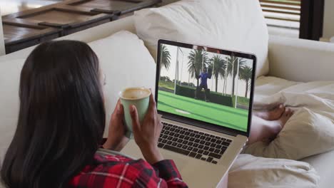 compuesto de una mujer sentada en casa sosteniendo un café viendo un partido de hockey en una computadora portátil