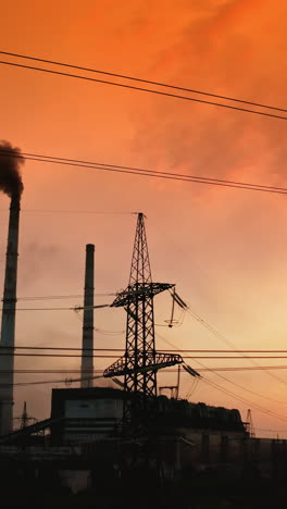 electrical pylons near harmful factory at red sunset. dark smoke released into the air from industrial pipe. transmission lines. pollution the environment. camera moving down. vertical video