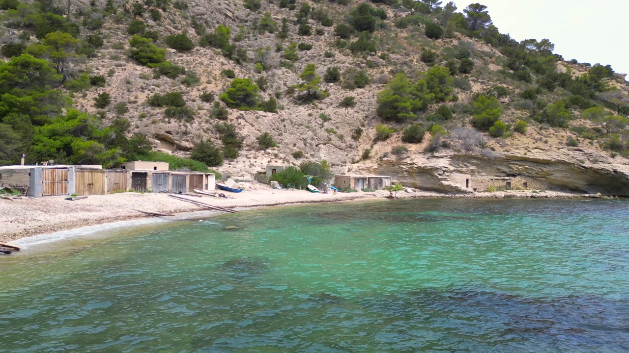Cala Llentrisca, a secluded beach in Ibiza, highlighting the pristine turquoise waters and surrounding verdant landscape. Breathtaking aerial view flight dolly right drone