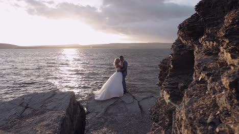 Newlyweds-couple-on-a-mountainside-by-the-sea.-Sunset.-Groom-and-bride