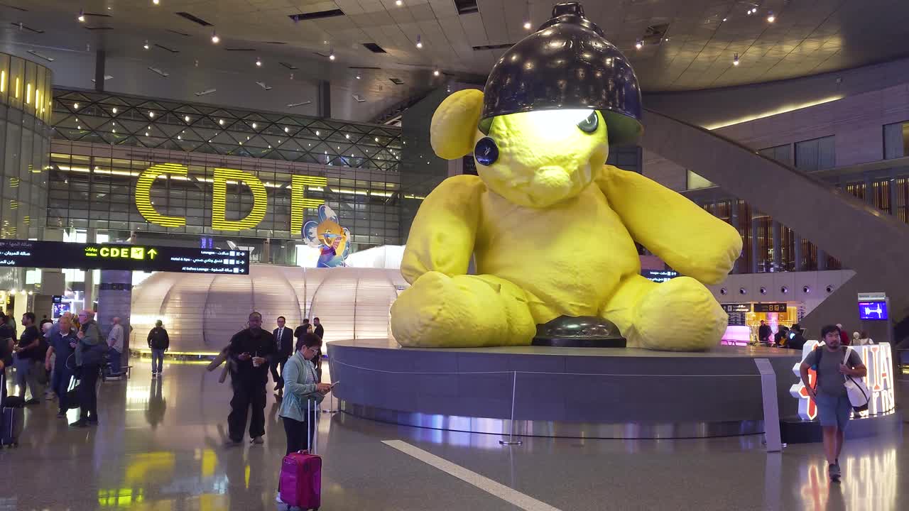 Passengers walking along the giant yellow Lamp Bear at Hamad International Airport - Doha, Qatar