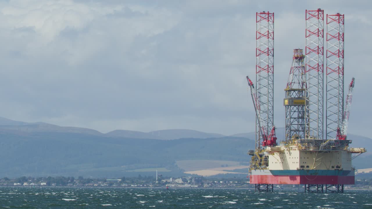 Stationary offshore oil drilling rig in choppy sea under cloudy sky, distant coastline visible