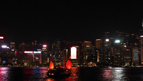 junk boat sails across illuminated city skyline