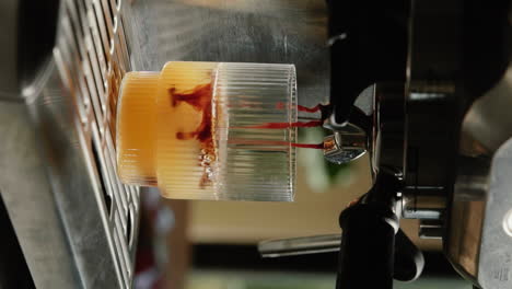 video vertical haciendo espresso naranja en casa extrayendo espresso de un portafiltro en un vaso de bebida a cámara lenta de cerca