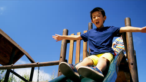 happy schoolboy playing on slide in playground